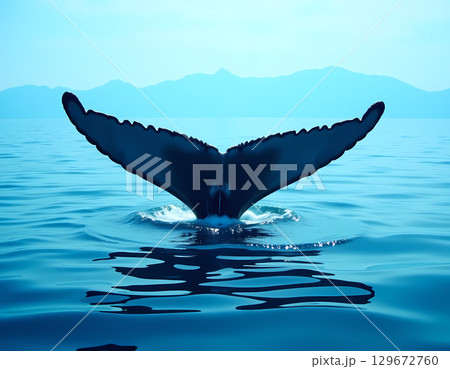 A powerful whale tail rises and splashes into serene waters, surrounded by tranquil ripples. The sun begins to rise, casting a magical glow over the landscape Generative AI 129672760