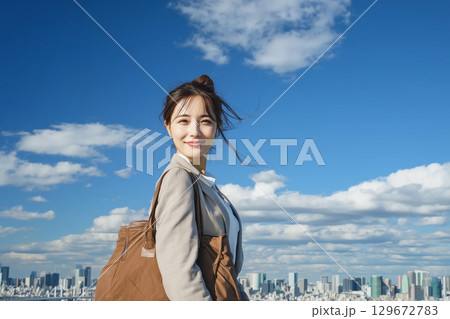 青空と街並みを背景に笑顔で立つ若い女性のライフスタイル 青空と街並みを背景に笑顔で立つ若い女性のライフスタイル 129672783