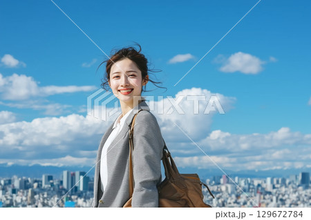 青空と高層ビル群を背景に笑顔の日本人の若い女性。ビジネスウーマン 129672784