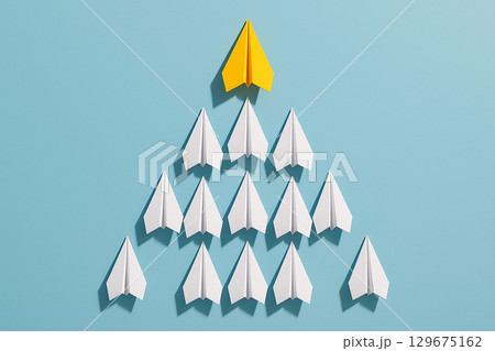 A yellow paper airplane positioned at the top of a triangular group of white airplanes representing leadership hierarchy A yellow paper airplane positioned at the top of a triangular group of white airplanes representing leadership hierarchy 129675162