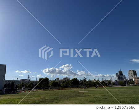夏の青空と広がる芝生の公園風景、白い雲と住宅街が広がる晴天の空、爽やかな快晴に包まれた都市の空と緑 夏の青空と広がる芝生の公園風景、白い雲と住宅街が広がる晴天の空、爽やかな快晴に包まれた都市の空と緑 129675666
