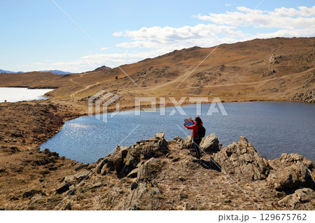 The girl travels around the island of Olkhon in the spring. Hilly terrain, heart-shaped lake. The girl travels around the island of Olkhon in the spring. Hilly terrain, heart-shaped lake. 129675762
