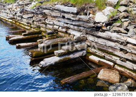 An old ruined pier made of tree logs near the lake shore An old ruined pier made of tree logs near the lake shore 129675776