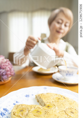 ケーキを焼いて紅茶を入れ自分時間を楽しむシニア女性 129675906