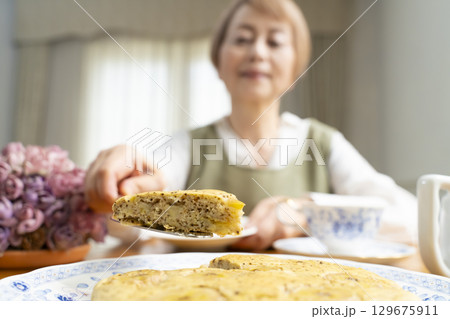 ケーキを焼いて紅茶を入れ自分時間を楽しむシニア女性 ケーキを焼いて紅茶を入れ自分時間を楽しむシニア女性 129675911