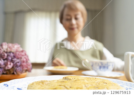 ケーキを焼いて紅茶を入れ自分時間を楽しむシニア女性 ケーキを焼いて紅茶を入れ自分時間を楽しむシニア女性 129675913