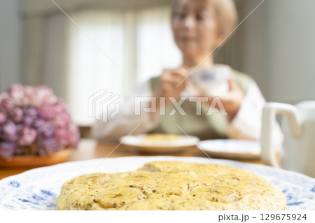 ケーキを焼いて紅茶を入れ自分時間を楽しむシニア女性 ケーキを焼いて紅茶を入れ自分時間を楽しむシニア女性 129675924