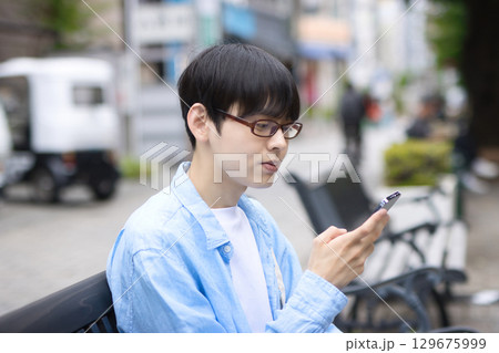 街中のベンチに座ってスマホを見る若い男性 街中のベンチに座ってスマホを見る若い男性 129675999