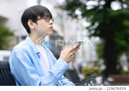 街中のベンチに座ってスマホを見る若い男性 街中のベンチに座ってスマホを見る若い男性 129676839