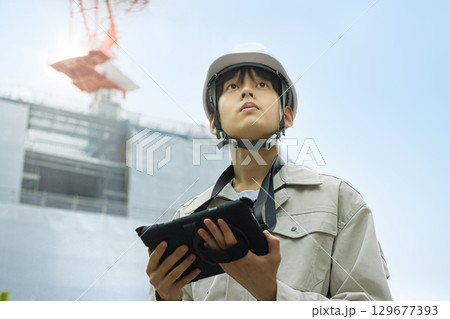 工事現場でタブレットを見る作業服の若いビジネスマン 工事現場でタブレットを見る作業服の若いビジネスマン 129677393