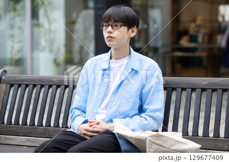 街中のベンチに座る若い男性 129677409