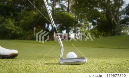 Golfer putting ball on the green golf, lens flare on sun set evening time. Golfer hitting golf ball. 129677890