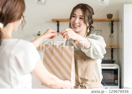 カフェ・飲食店でテイクアウトの商品を客に渡す女性カフェ定員 129678936