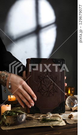 Female hands take old grimoire from a table with magic tools, vertical photo, copy space. Female hands take old grimoire from a table with magic tools, vertical photo, copy space. 129679077