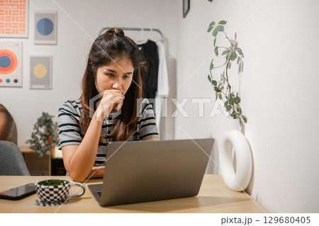 A young woman concentrating on her laptop in a stylish home office with modern decor and minimalist design. A young woman concentrating on her laptop in a stylish home office with modern decor and minimalist design. 129680405