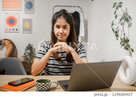 Young woman in a home office setting with a laptop, smartphone, and modern decor, exuding confidence and focus. Young woman in a home office setting with a laptop, smartphone, and modern decor, exuding confidence and focus. 129680407