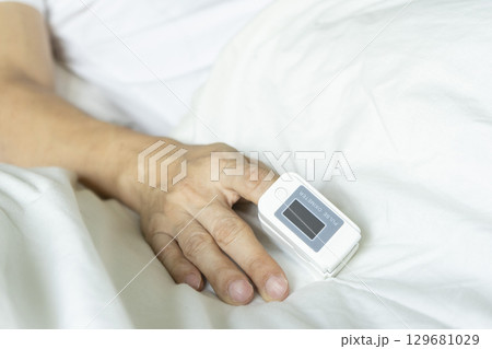 Cropped view of male patient using oximeter on finger lying in bed. 129681029