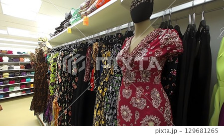 Mannequin in floral dress stands among diverse dresses in a well 129681265