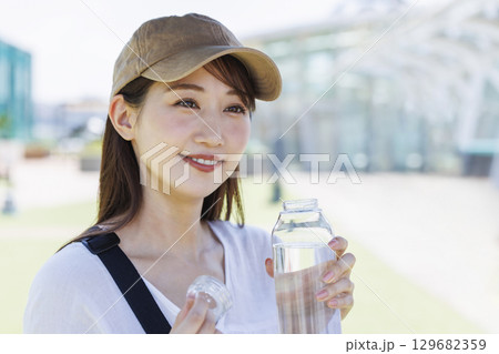 屋外で水分補給をするキャップを被った女性 屋外で水分補給をするキャップを被った女性 129682359
