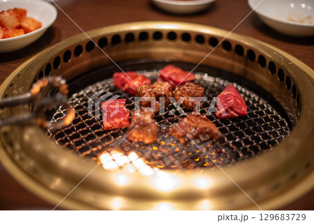 Close-up of meat grilling on a Korean barbecue grill with tongs Close-up of meat grilling on a Korean barbecue grill with tongs 129683729