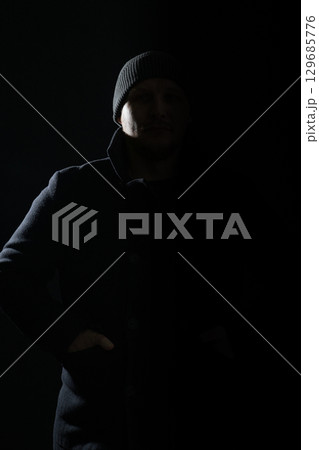Man with coat and hat hiding in shadow and silhouette illuminate with light 129685776