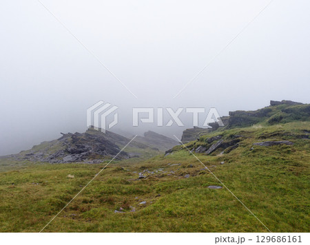 The Rocky Mountains, covered in grass and small plants, are almost completely covered in thick fog. The low visibility means it is a cloudy, overcast day in the Irish landscape. 129686161