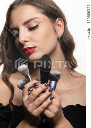 Beautiful woman with make-up brushes and red lips studio portrait Beautiful woman with make-up brushes and red lips studio portrait 129686228