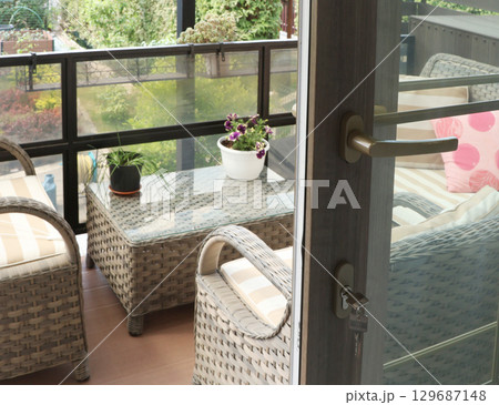 Wicker furniture on a wooden terrace on a sunny summer day. Open modern sliding door. Leisure and lifestyle. Wicker furniture on a wooden terrace on a sunny summer day. Open modern sliding door. Leisure and lifestyle. 129687148