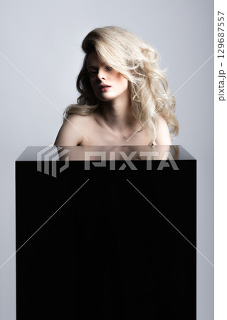 Beautiful woman with big wavy hair and black cube studio portrait 129687557