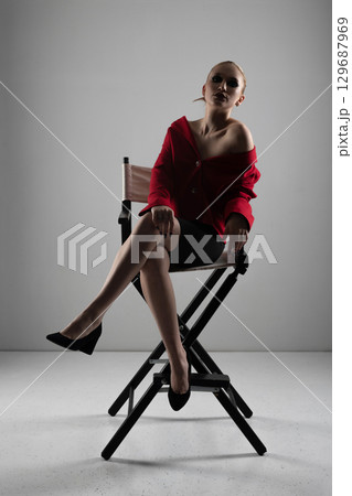 Beautiful woman with red jacket and mini shirt sitting in high chair 129687969