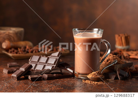 Pieces of bitter chocolate and glass of cocoa drink on a brown table. 129688317