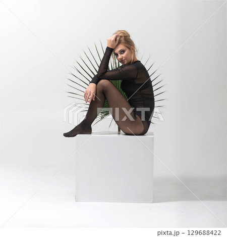 Portrait of beautiful woman with tight black clothes sitting on white cube 129688422