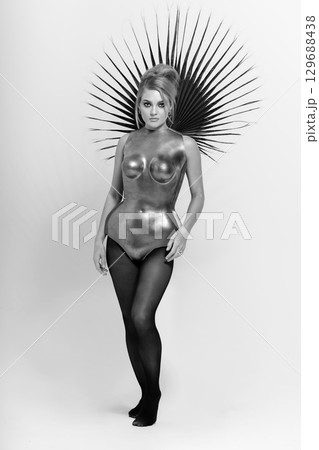 Beautiful woman with metallic corset and palm leaf black and white studio portrait Beautiful woman with metallic corset and palm leaf black and white studio portrait 129688438