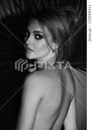 Beautiful woman with naked back and palm leaf black and white studio portrait Beautiful woman with naked back and palm leaf black and white studio portrait 129688451