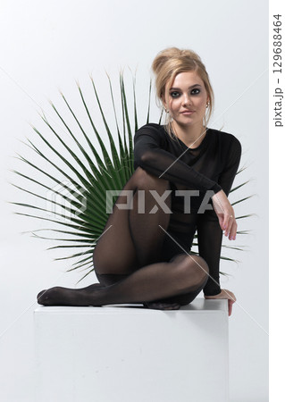 Portrait of beautiful woman with tight black clothes sitting on white cube Portrait of beautiful woman with tight black clothes sitting on white cube 129688464