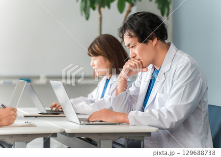 デスクに座り仕事する白衣姿の男女の医師,ドクター 129688738
