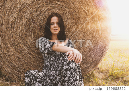 Woman Sitting by Hay Bale at Sunset Woman Sitting by Hay Bale at Sunset 129688822