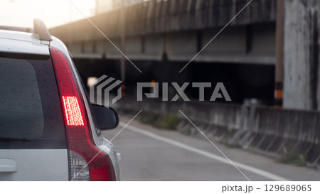Rear side of aline white car with turn on brake light. Driving on the road to work or home or traveling. Background cement bridge overpass and bright sky. 129689065