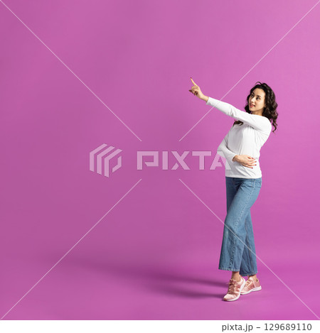 Woman pointing with finger to blank zone on purple background 129689110