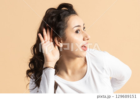 Woman listening with one hand placed near her ear 129689151