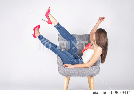 Woman with pink shoes and jeans lying on armchair 129689434