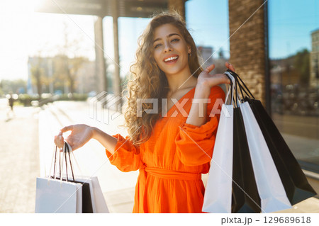 Young woman with shopping bags near mall. Purchases, shopping, lifestyle, sale concept. 129689618
