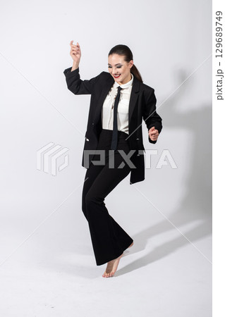 Woman wearing classic black suit and dancing on studio white background 129689749