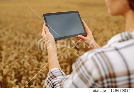 Woman agronomist in a field with a tablet checks the growth of the crop. New harvest concept. Woman agronomist in a field with a tablet checks the growth of the crop. New harvest concept. 129689854