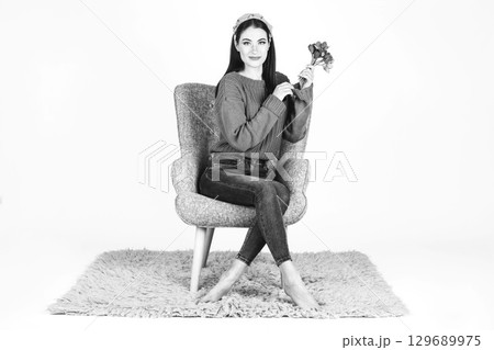 Woman with sweater, jeans and flowers sitting on armchair Woman with sweater, jeans and flowers sitting on armchair 129689975