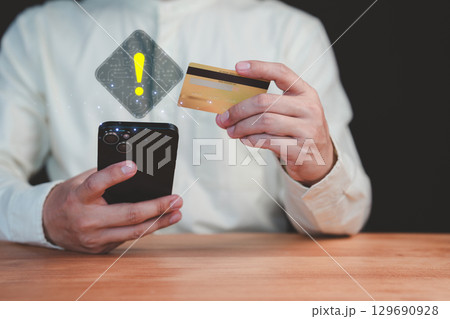 Adult man holding a credit card and mobile phone with a warning sign overlay, symbolizing online scams, fraud, security risks, transfer money and financial caution in digital transactions. 129690928