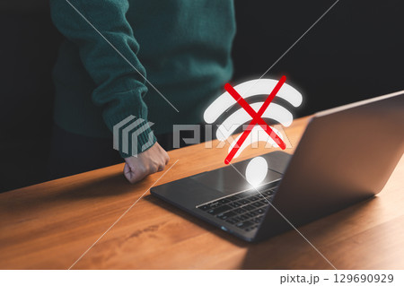 User using a laptop to connect to wifi with a crossed-out Wi-Fi symbol, representing internet disconnection and network failure stress. Concept of frustrated user waiting for connect to wifi. 129690929