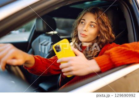 Woman sitting in a car looking into a smartphone, paying for parking and navigating in the city. 129690992