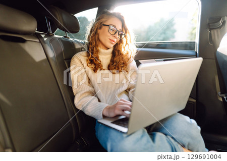 Young woman in glasses with a laptop in the back seat of a car. Freelance, business concept. Young woman in glasses with a laptop in the back seat of a car. Freelance, business concept. 129691004
