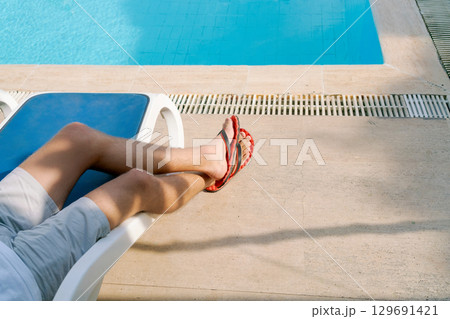 Man is laying on a lounge chair by a pool 129691421